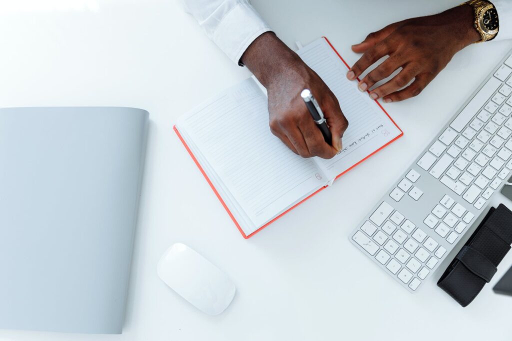 person writing on white paper beside apple magic mouse